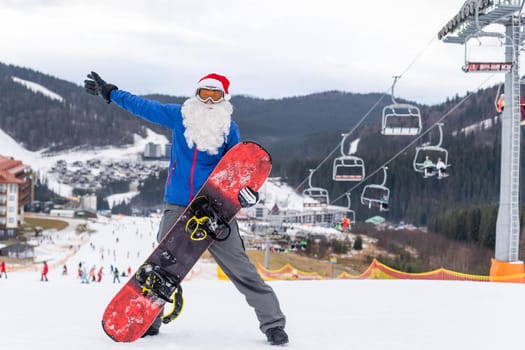 happy man in santa red christmas hat with snowboard at winter mountains hill.