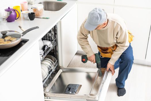 View Of Man In Overall Repairing Dishwasher In Kitchen.