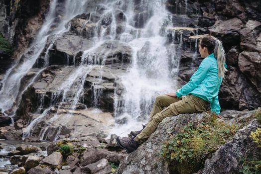 Traveler young woman sitting on stone and enjoying view of waterfall outdoor