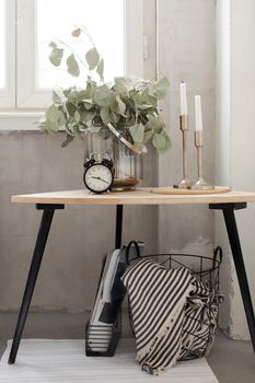 Beautiful arrangement with green plant branches candles and alarm clock on small table