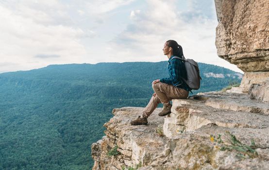 Explorer young woman sitting high on cliff Eagle shelf and enjoying view of nature in summer, Mezmay, Krasnodar region, Russia
