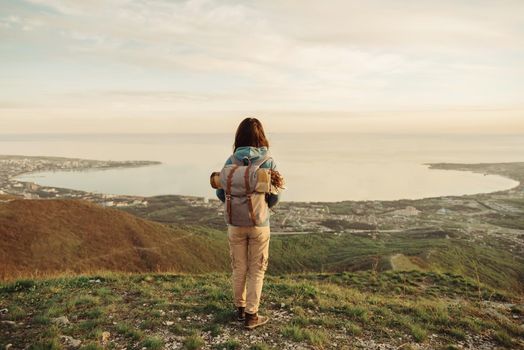 Traveler explorer young woman with backpack standing on peak of mountain and enjoying view of sea bay