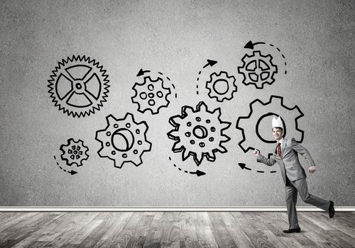 Young handsome businessman wearing white paper crown running and gear mechanism on wall