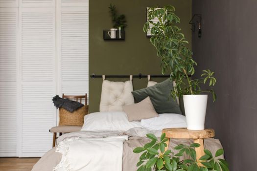 Plants grow in pots on a wooden stool. Bedroom in scandinavian style. Grey knitted quilt