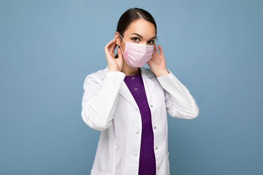 Beautiful young woman holds and wears a white medical mask to protect yourself from corona virus, cares for her health and safety, sticks to self-isolation. Concept of Covid-19.