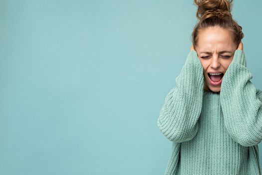 Closeup portrait of young emotional attractive blonde woman with sincere emotions wearing casual blue jersey isolated over blue background with empty space and shouting.