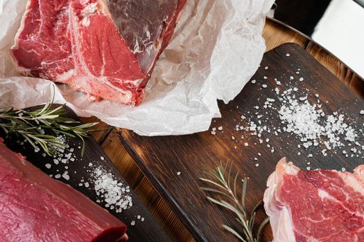 Raw T-bone steak with herbs on wooden board, close up