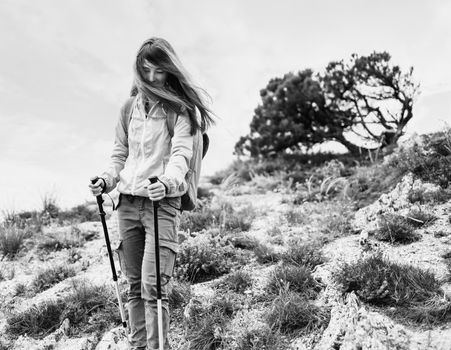 Beautiful hiker young woman with backpack and trekking poles walking in the mountains in summer outdoor. Monochrome image