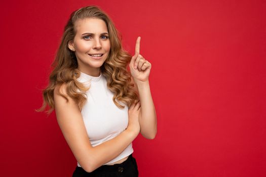 Photo of attractive amazed surprised young woman pointing finger up at copyspace presenting ads promo with wow omg sincere emotions wearing good look outfit isolated over background with free space.