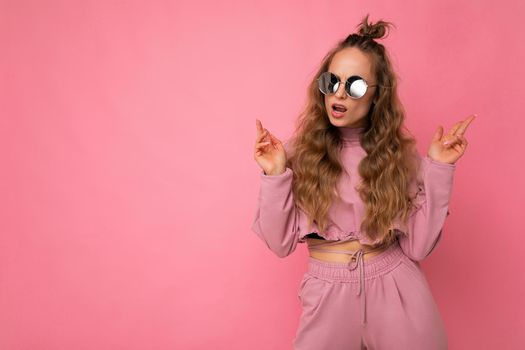 Attractive sexy self-confident young blonde woman wearing everyday stylish clothes and modern sunglasses isolated on colorful background wall looking to the side. copy space