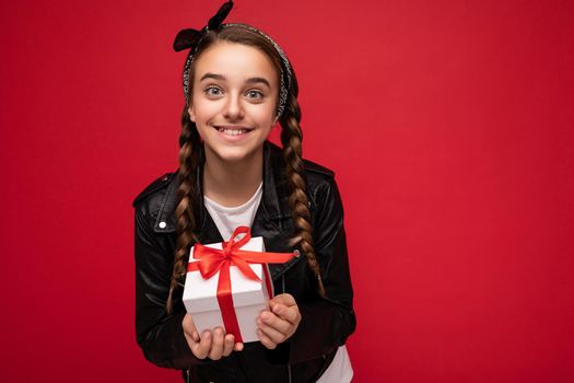 Beautiful happy brunette girl isolated over colourful background wall wearing stylish casual clothes holding gift box and looking at camera.