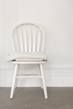 White old-fashioned retro style chair standing in an empty room in front of a wall on light parquet floor. Natural light from the window