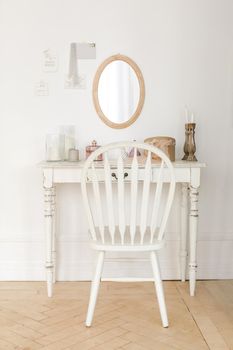 Interior shot of small boudoir dressing table with small mirror and white wooden chair.