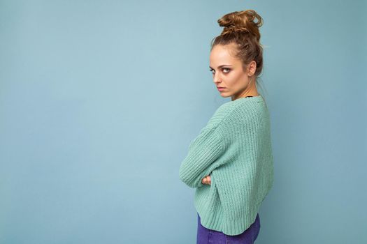 Photo of young attractive european fashion blonde woman wearing blue sweater isolated over blue background with copy space with serious expression on face. Simple and natural female person.