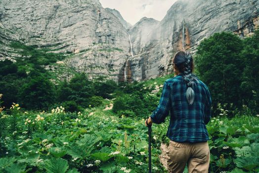 Traveler young woman goes to the waterfalls in rocky mountains in summer, rear view