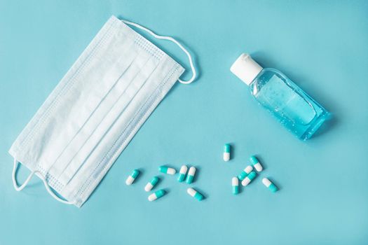 Respiratory mask, atibacterial hand treatment and medicine in capsules on blue background.Virus prevention and treatment.