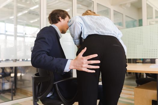 Back view of man molesting young girl at work putting hand on her bottom while working at table