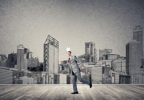 Young handsome businessman wearing white paper crown running in a hurry