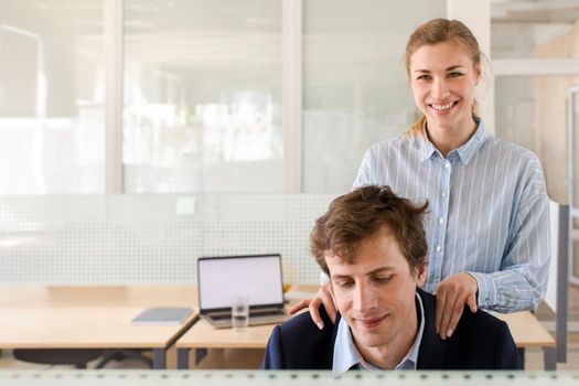 Crop view of attractive smiling female doing neck massage for sitting man in suit on working place