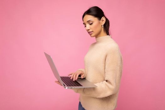 side profile photo of charming pretty young lady holding laptop isolated over wall background looking at netbook typing on keyboard text and thinking about something.