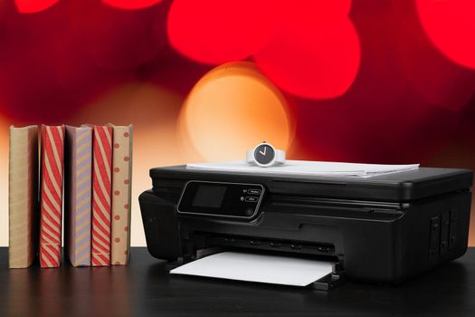 Stack of books and home printer against blurred background, close up