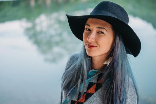 Portrait of smiling beautiful woman with blue hair in the hat on background of lake