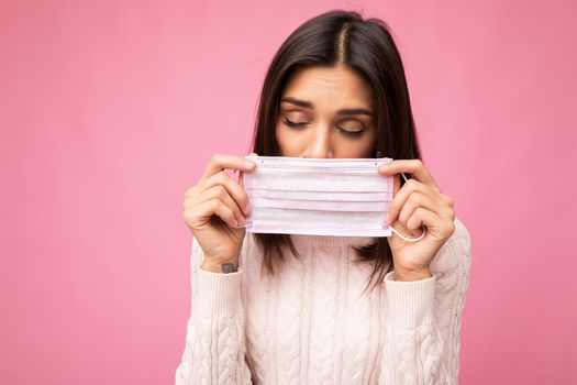 Upset young woman holds and wears a white medical mask to protect yourself from corona virus, cares for her health and safety, sticks to self-isolation. Concept of Covid-19.
