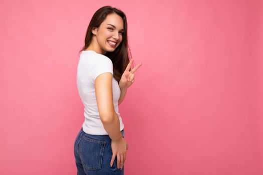 Photo portrait of young beautiful smiling hipster brunette woman in white t-shirt with mockup. Sexy carefree female person posing isolated near pink wall with empty space in studio. Positive model with natural makeup.