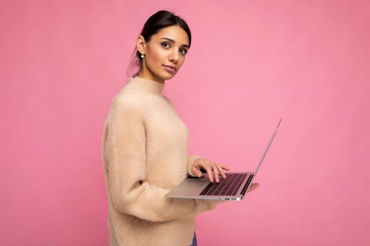side profile photo of charming pretty young woman holding laptop isolated over wall background looking at camera typing on keyboard text and thinking about something.