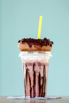 Chocolate and donuts extreme milkshakein a plastic cup on blue background. Crazy freakshake or overshake on wooden table with copy space