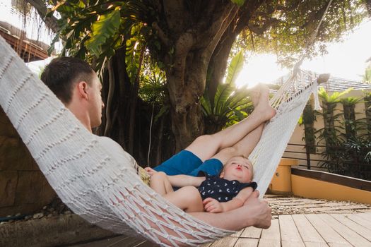 Cute adorable baby boy of 18 months and his father sleeping peaceful in hammock in outdoor garden