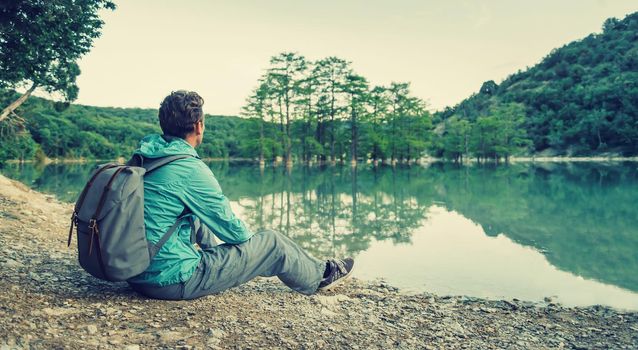 Traveler young man with backpack resting on shore of lake. Toned image