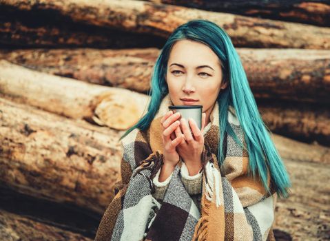 Young woman wrapped in plaid drinking tea outdoor