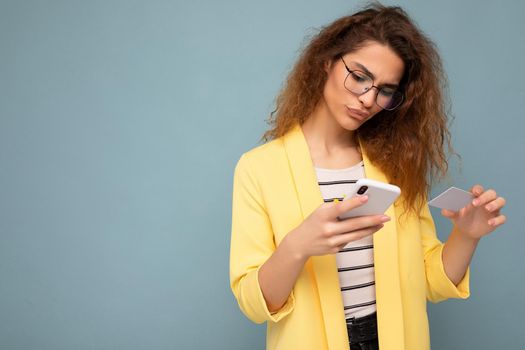 Young woman wearing everyday clothes isolated over background holding phone and credit card paying online shopping through credit card looking at smartphone screen.