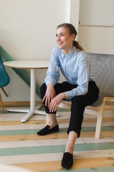 Full body of female worker laughing happily at spare time in modern workplace while looking away