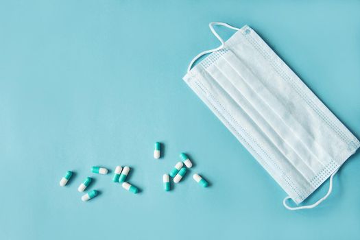 Respiratory mask and medicine in capsules on blue background.Virus prevention and treatment.
