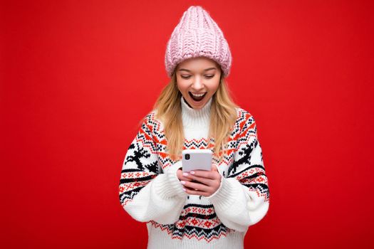 Photo of attractive crazy amazed surprised young woman wearing casual stylish clothes standing isolated over background with copy space holding and using mobile phone looking at device display.