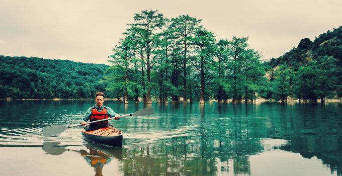 Young man kayaking on lake on background of beautiful cypresses in summer. Toned image