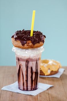 Chocolate and donuts extreme milkshakein a plastic cup on blue background. Crazy freakshake or overshake on wooden table with copy space