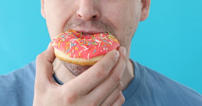 Man is eating a pink donut closeup on a blue background