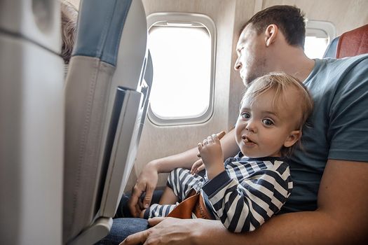 Man with little adorable boy on knees sitting near window in plane flying.