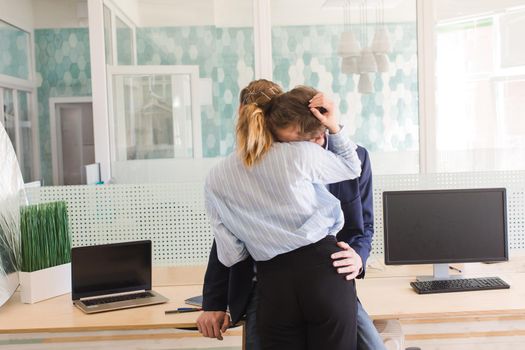 Back view of unrecognizable passionate man and woman embracing and kissing at desk in office