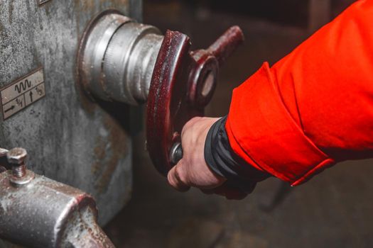 The hand of a man worker in a suit controls the milling machine by the handle in an industrial plant.