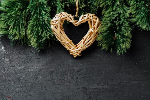 Fir tree branches with wooden heart on black , christmas background
