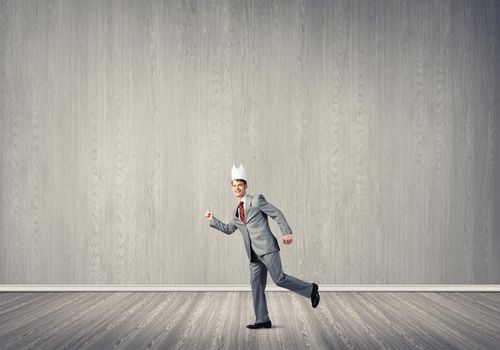 Young handsome businessman wearing white paper crown running in a hurry