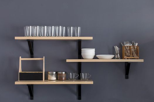 Stylish shelf with various dishware hanging on gray wall.