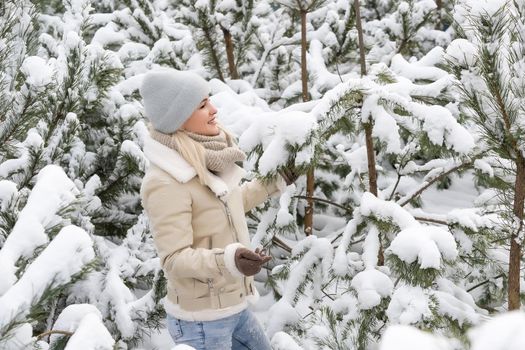 A girl in white clothes stands near a pine tree in the snow. Image with selective focus and toning.