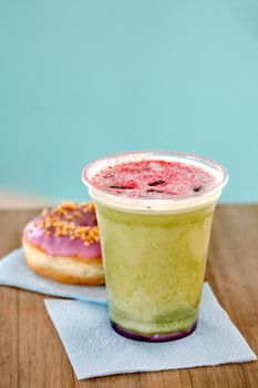 Green tea matcha smoothies in a plastic cup with berries and donut in interior