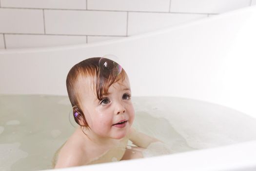 Adorable bath baby boy with soap suds soap bubble on hair laughs