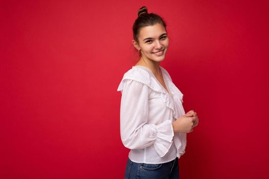 Young beautiful european stylish brunette woman wearing white blouse isolated over red background with positive sincere emotions. Simple and natural looking at the camera. Free space.